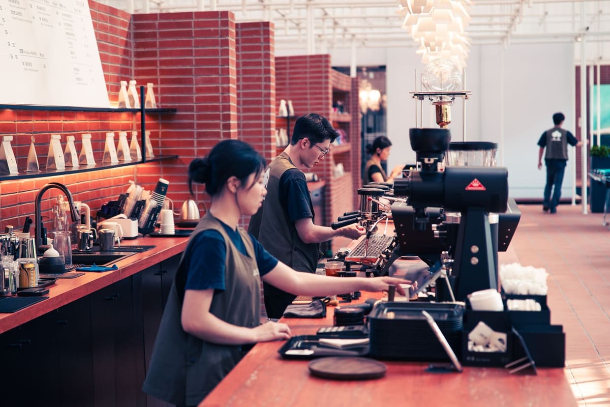 Baristas in aprons working along a cafe counter, making coffee at an espresso machine during service