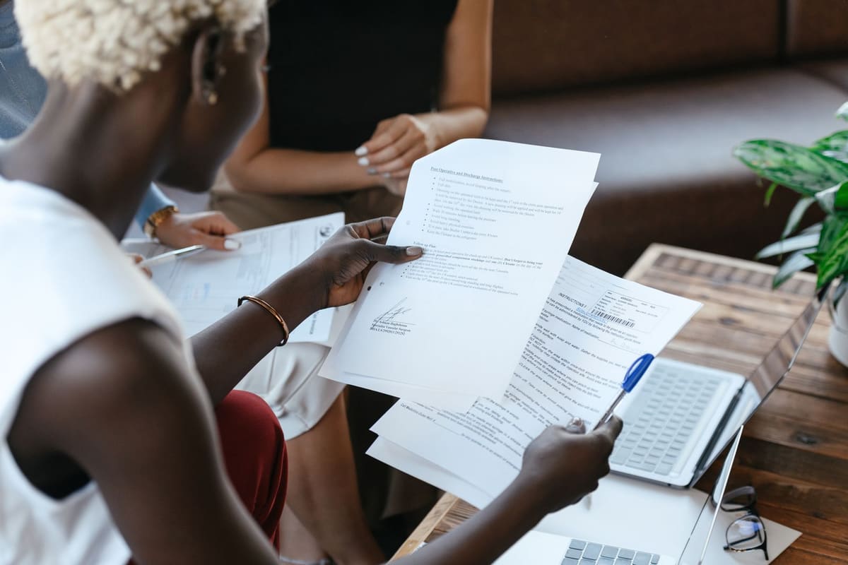 A person at a desk holding up printed documents to compare them, with a calculator and further papers alongside