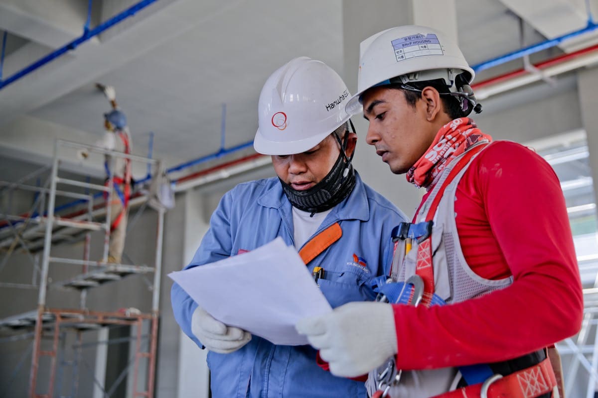 Two workers in hard hats reviewing a document on a construction site