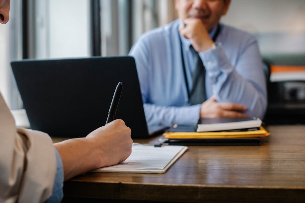 A person reviewing documents at a desk beside an open laptop