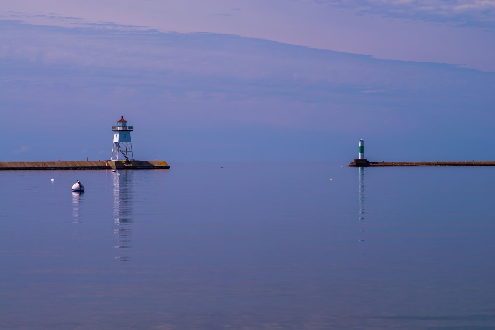 A harbour breakwater and lighthouse at dusk, with still water in the foreground