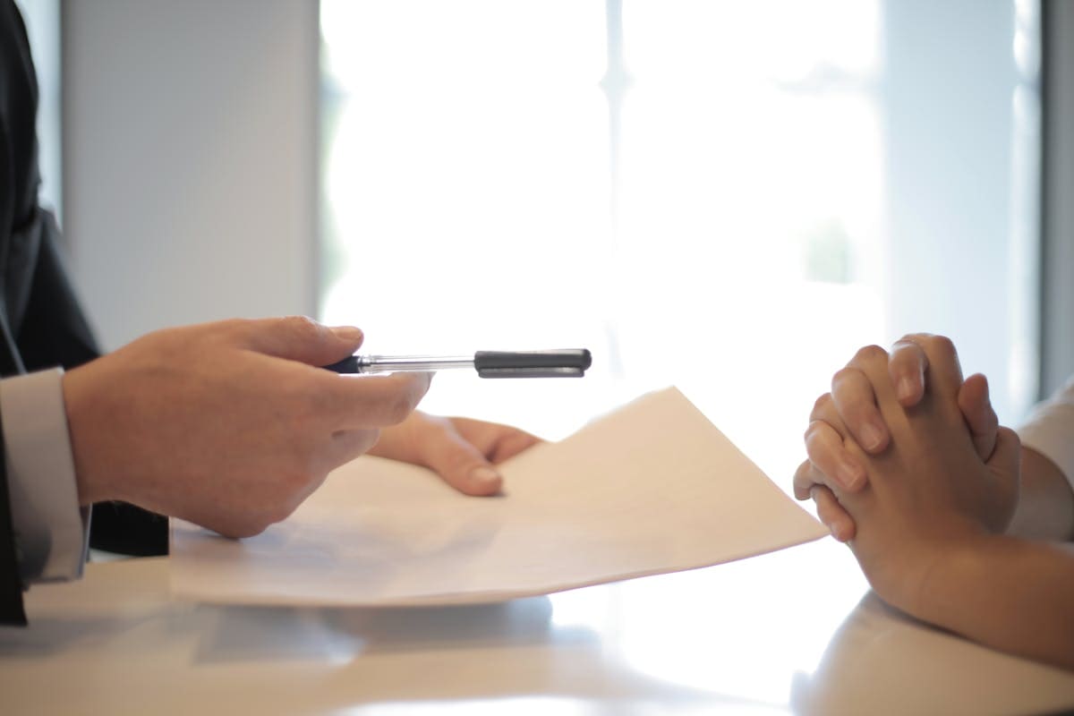 Two people at a table, one passing a document across to the other