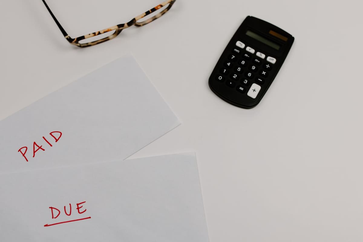 Two handwritten sheets reading “PAID” and “DUE” in red, beside a black calculator and a pair of glasses