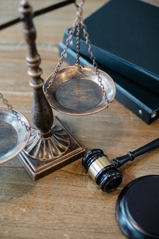 Brass scales of justice on a desk with a gavel and law books behind