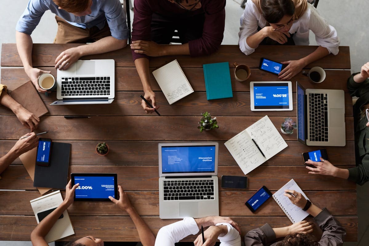 Overhead view of a table with laptops, notebooks and people working through a plan